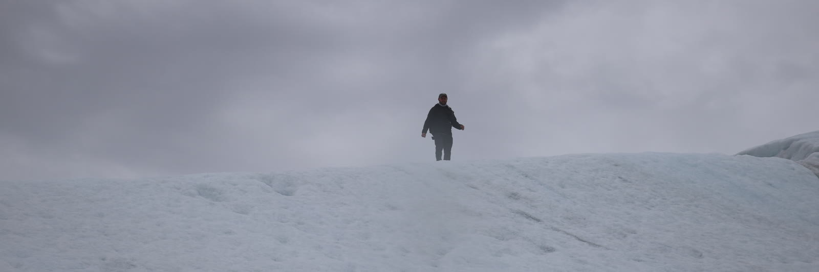 Caleb walking a glacier ridge under heavy overcast cloud
